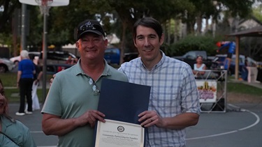 Two men smiling while holding a certificate of recognition at a community event