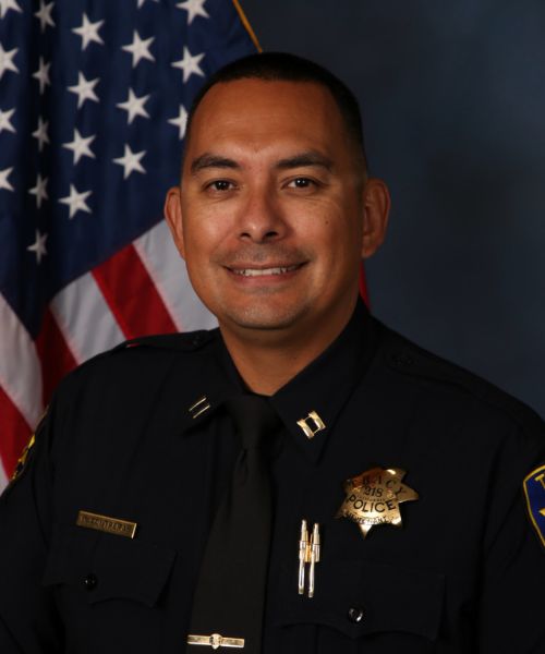 Portrait of a Tracy Police officer in uniform standing in front of an American flag.