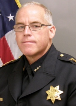 Color portrait of a Tracy police chief in uniform with an American flag in the background.