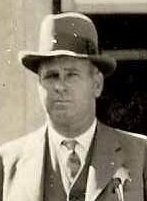 Historic black-and-white portrait of a man wearing a suit, tie, and brimmed hat.