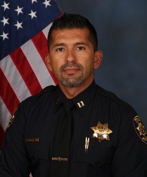 Portrait of a Tracy Police officer in uniform standing in front of an American flag.