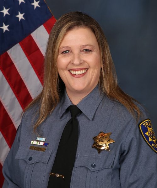Portrait of a Tracy Police officer in uniform standing in front of an American flag.