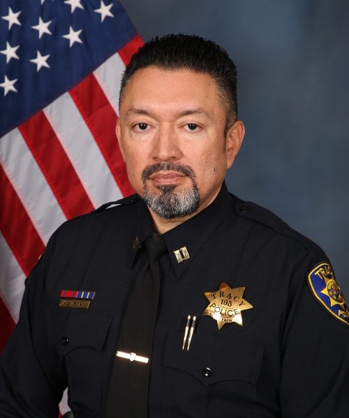 Portrait of a Tracy Police officer in uniform standing in front of an American flag.