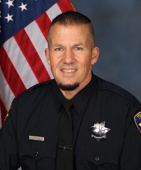 Portrait of a Tracy Police Department school resource officer in uniform with an American flag in the background.