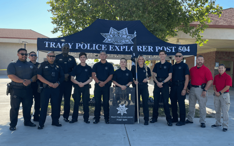 Tracy Police officers and youth Explorers posing together in front of the Tracy Police Explorer Post 504 tent.