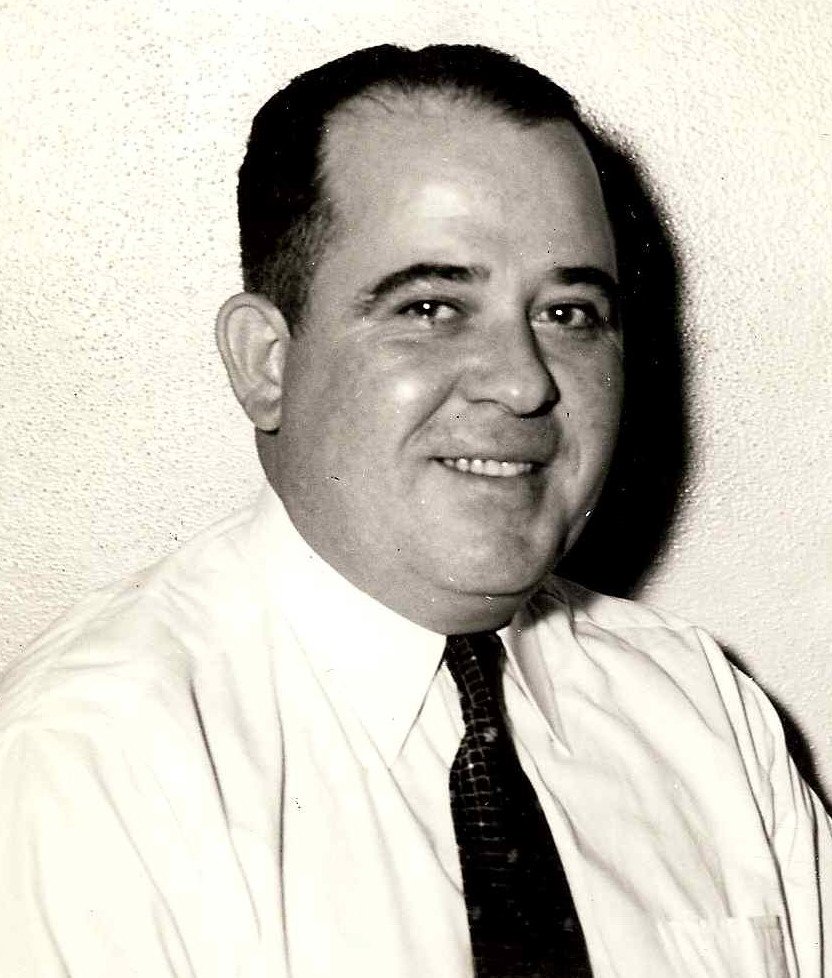 Historic black-and-white portrait of a smiling man wearing a dress shirt and tie.