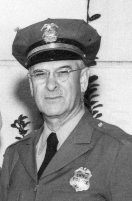 Black-and-white portrait of a uniformed Tracy police chief wearing a peaked cap and glasses.