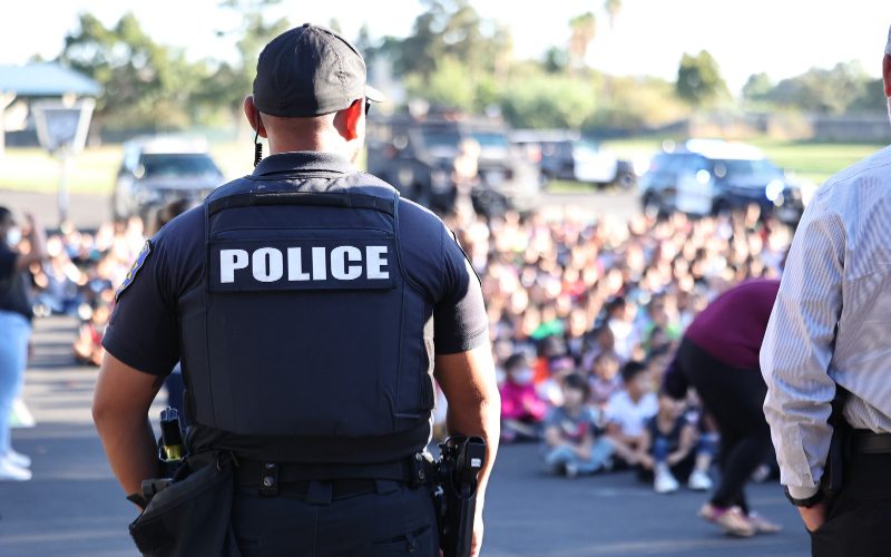 Tracy police officer facing a large group of students gathered outdoors.